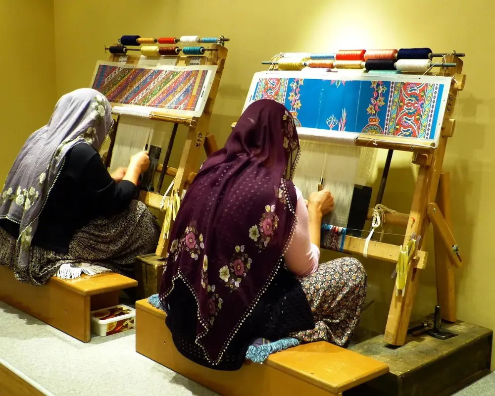 Two women creating hand-woven textiles on upright looms